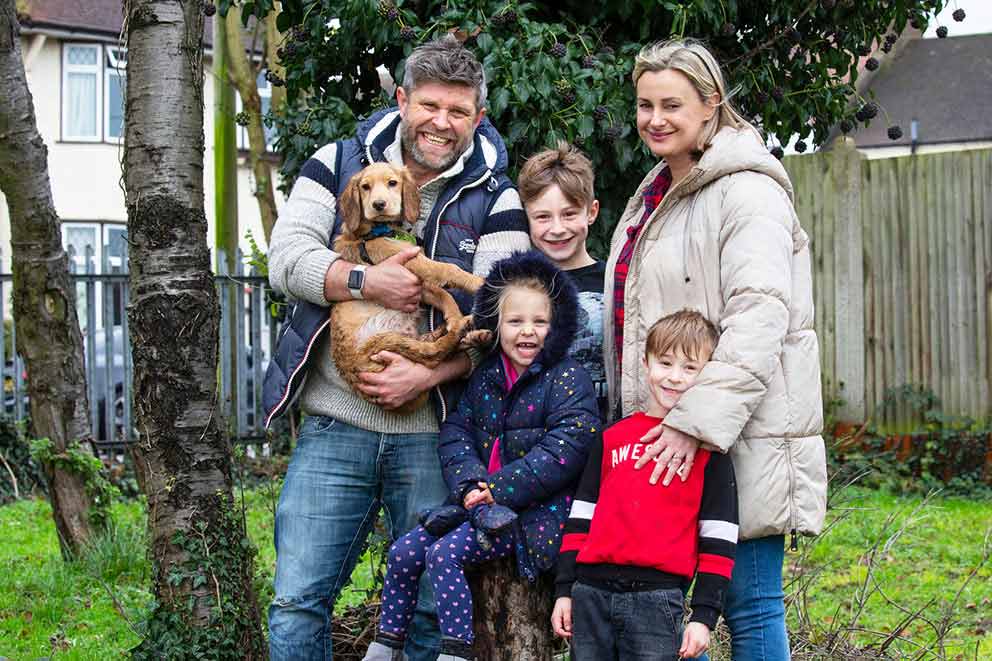 A family of five are gathered outside for a photo with their small golden dog