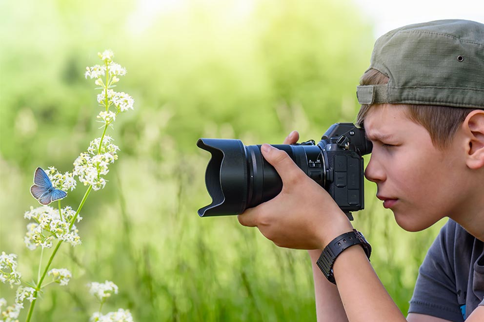 A young boy taking a close-up photograph of a butterfly.
